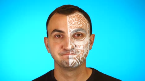 man with painted face is saying yes by shaking head against blue background