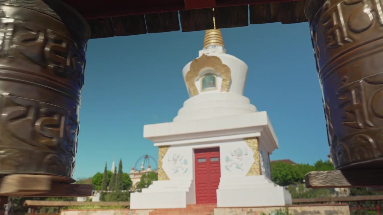 Tracking shot mellem to buddhistiske bedehjul mod tempel på en solrig dag