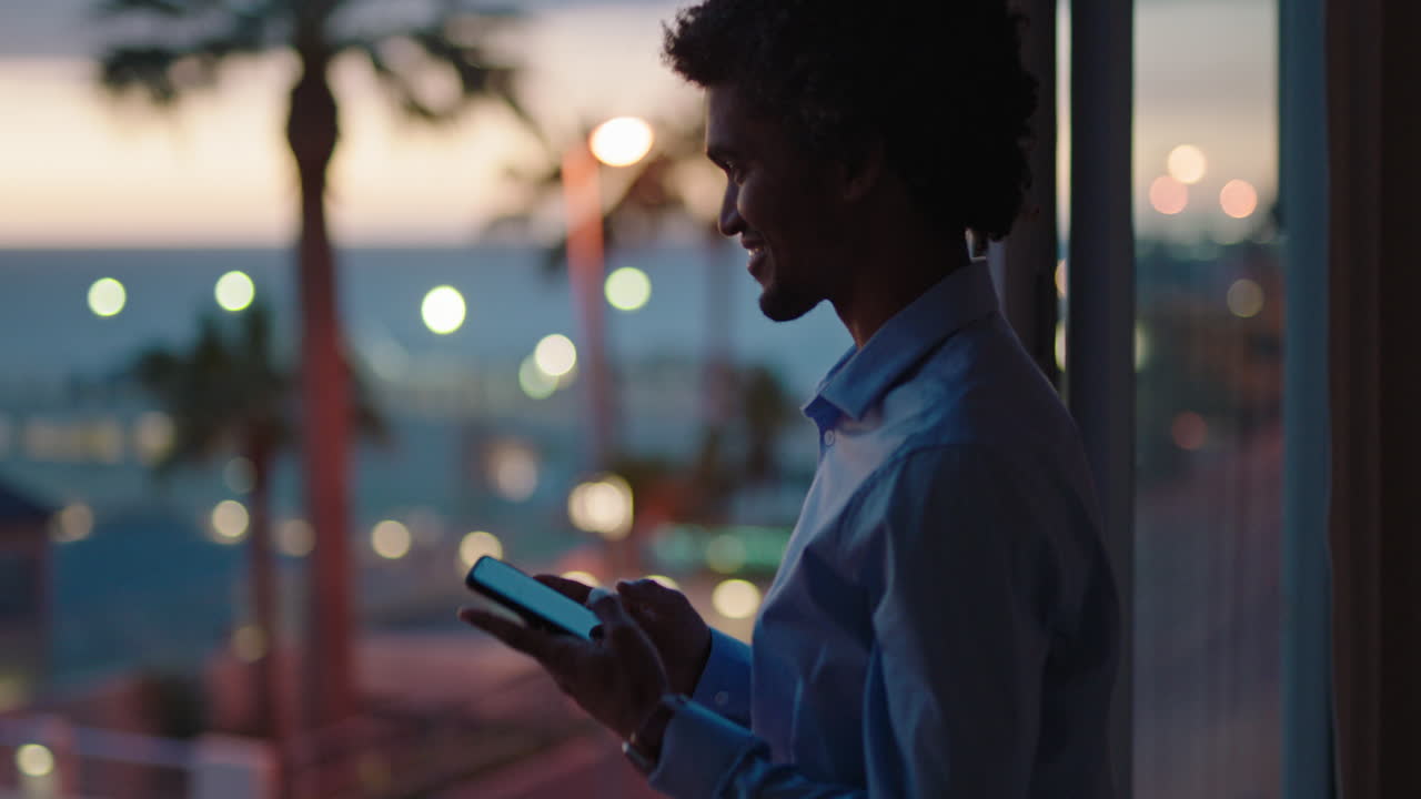 giovane uomo che usa lo smartphone in una stanza d'albergo che scrive messaggi condividendo lo stile di vita delle vacanze sui social media godendosi la vista dell'oceano al tramonto