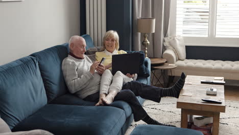 senior couple relaxing on couch with laptop and smartphone