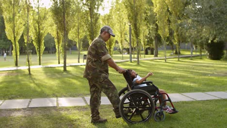 military dad walking with daughter in wheelchair and son at the park