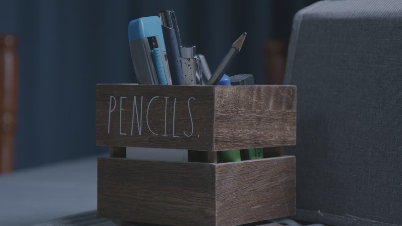 A cinematic close-up of a rustic wooden pencil holder on a desk, filled with pens and pencils. This ungraded LOG footage is perfect for a warm, focused, or moody scene