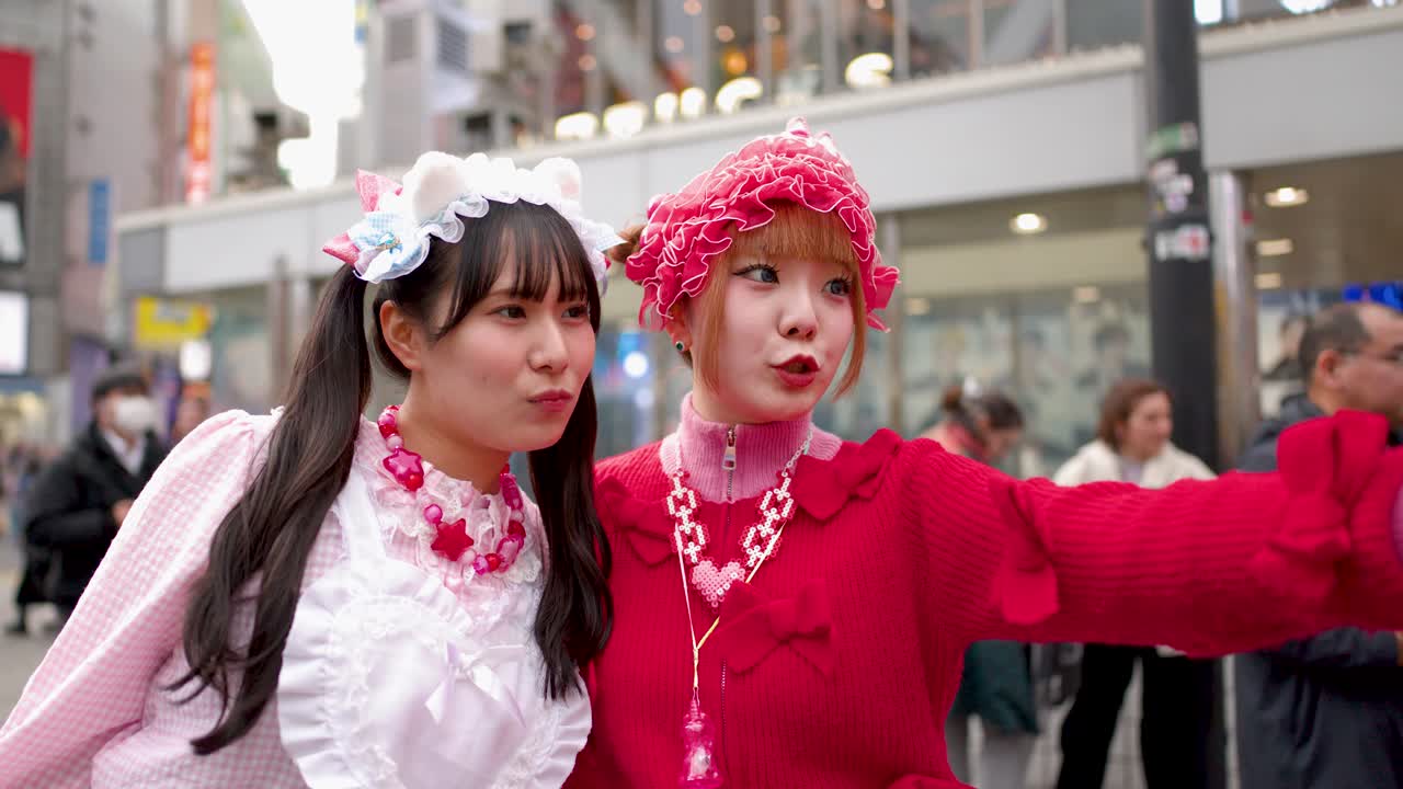 Duas mulheres com o colorido estilo de rua Decora tiram selfies em uma movimentada rua de Shibuya.
