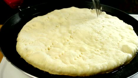 chef makes holes with fork in fresh flatbread, which is fried in hot pan in olive oil, for better frying.