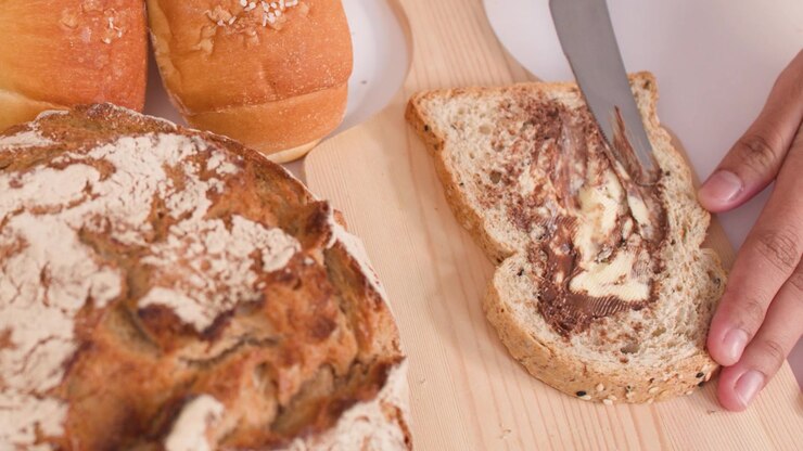 A close-up shot shows a knife spreading chocolate peanut butter on multigrain bread.