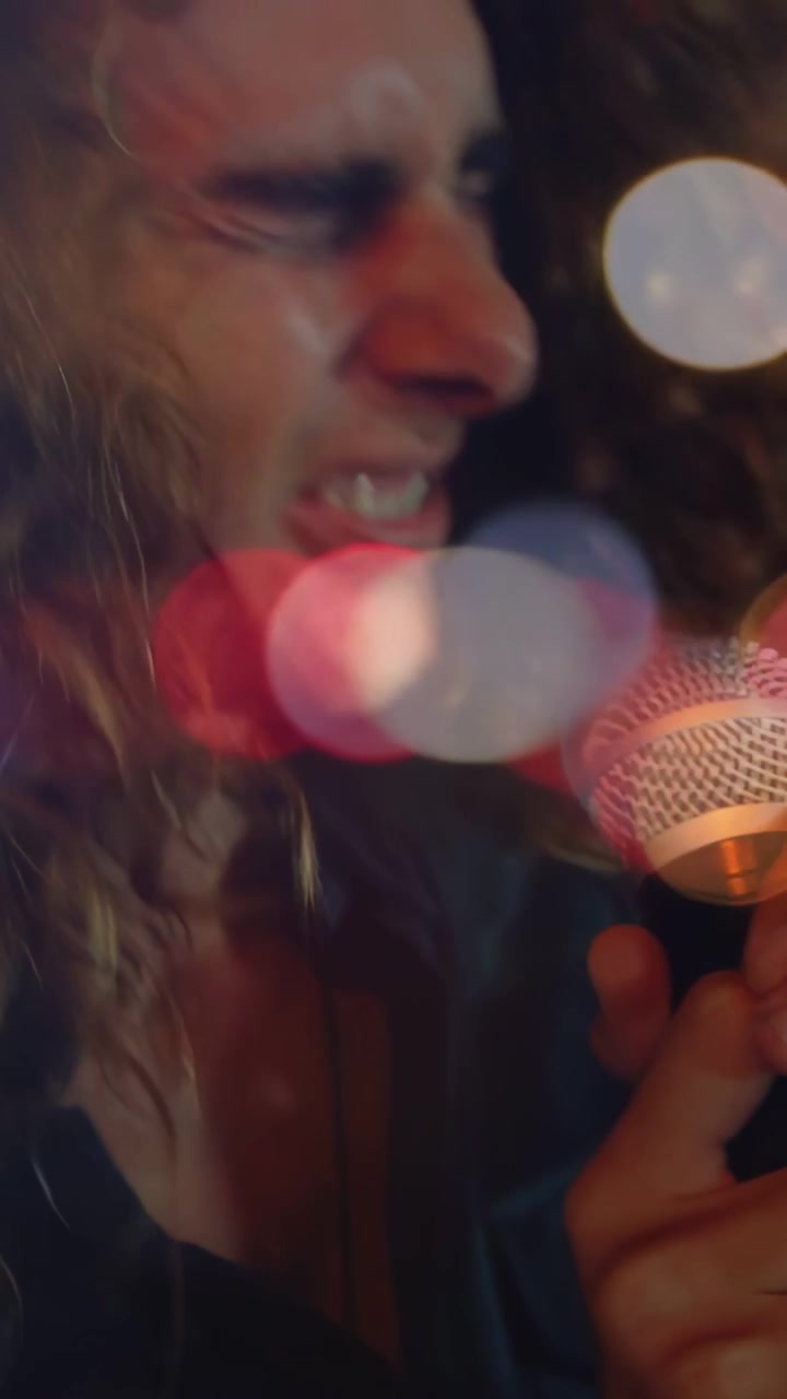 Vertical video: Male singer pressing mic and singing on music stage, moving bokeh adding raw energy