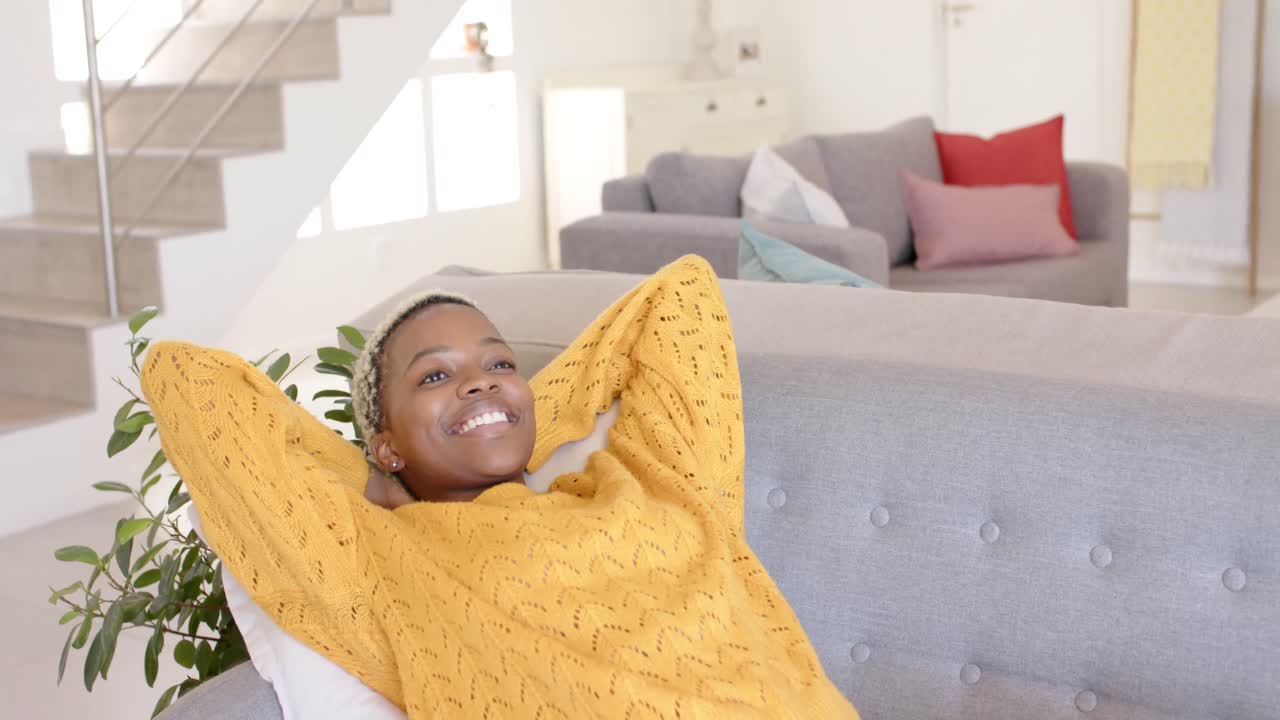 Happy african american woman lying on couch in living room in slow motion