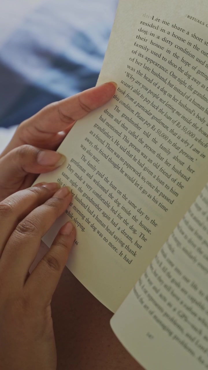 Close-up of a woman's hand gently pressing and smoothing an open book page while reading, with clearly visible printed text and soft natural window light illuminating.
