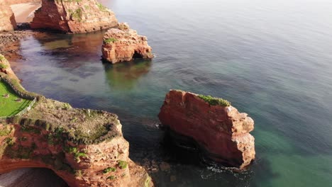 Majestätische,-Nach-Oben-Geneigte-Luftdrohnenaufnahme-über-Dem-Klaren-Und-Glitzernden-Wasser-Mit-Großen-Und-üppigen-Felsnadeln-Entlang-Der-Klippe-Der-Ladram-Bay