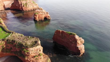 majestuoso dron aéreo inclinado hacia arriba disparó sobre las aguas claras y relucientes con grandes y exuberantes pináculos de roca a lo largo del acantilado de la bahía de ladram