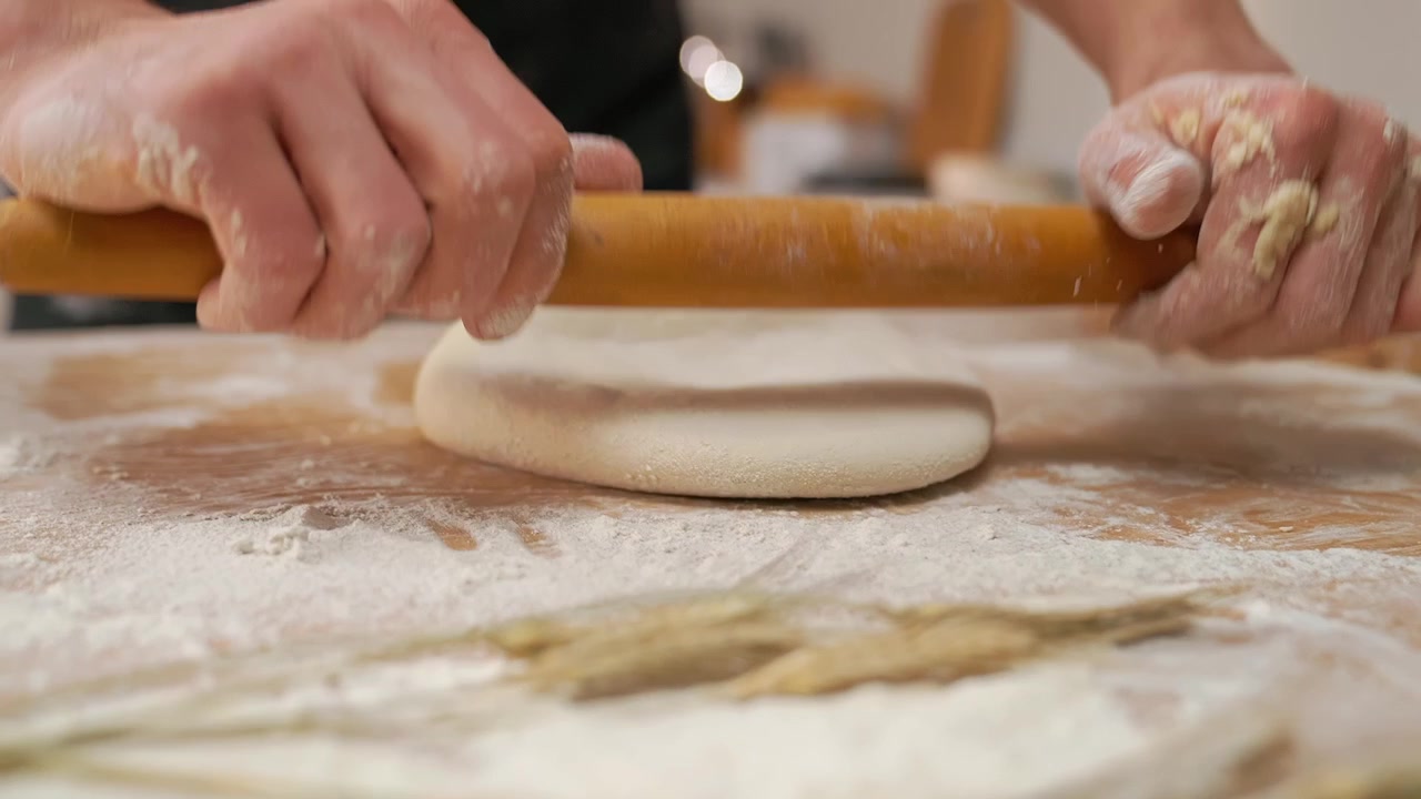 Primo piano di mani che stendono l'impasto con un mattarello di legno su un tavolo infarinato