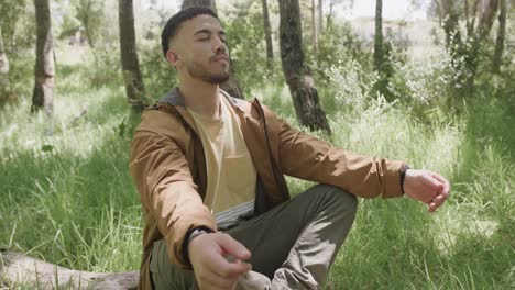 African-american-man-sitting-on-tree-trunk-and-meditating-in-forest,-slow-motion