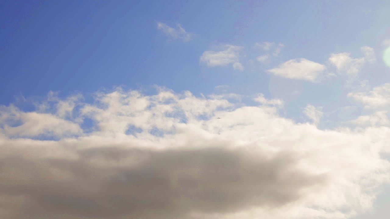 Extreme low angle following plane through blue and cloudy sky with slight lens flare. Tilting down to keep in frame.