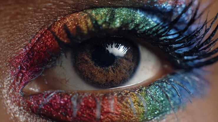 Close-up van een oog met levendige regenboog-make-up, glitterende eyeliner en lange wimpers, waarbij prachtige artistieke expressie en creativiteit worden benadrukt