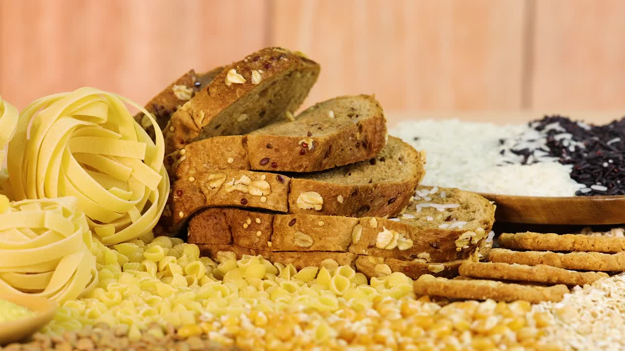 A variety of grains, pasta, and bread arranged on a wooden table with warm lighting