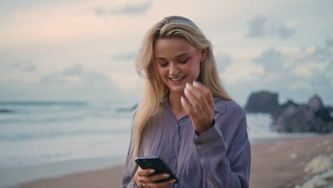 smiling girl checking sms on rocky shore closeup. relaxed tourist messaging cell