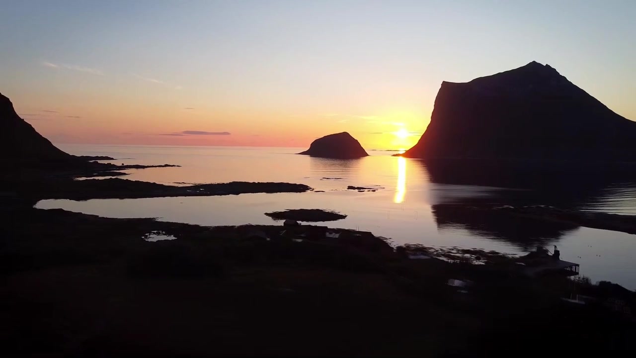 Silhueta de montanhas e falésias ao pôr do sol sobre a baía de mar calmo na ilha de Vaeroy, Lofoten, Noruega.