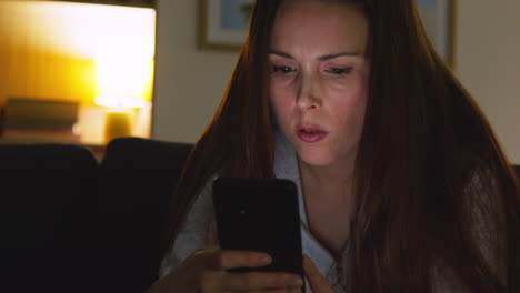 anxious woman sitting on sofa at home at night looking at mobile phone concerned about social media or bad news 3