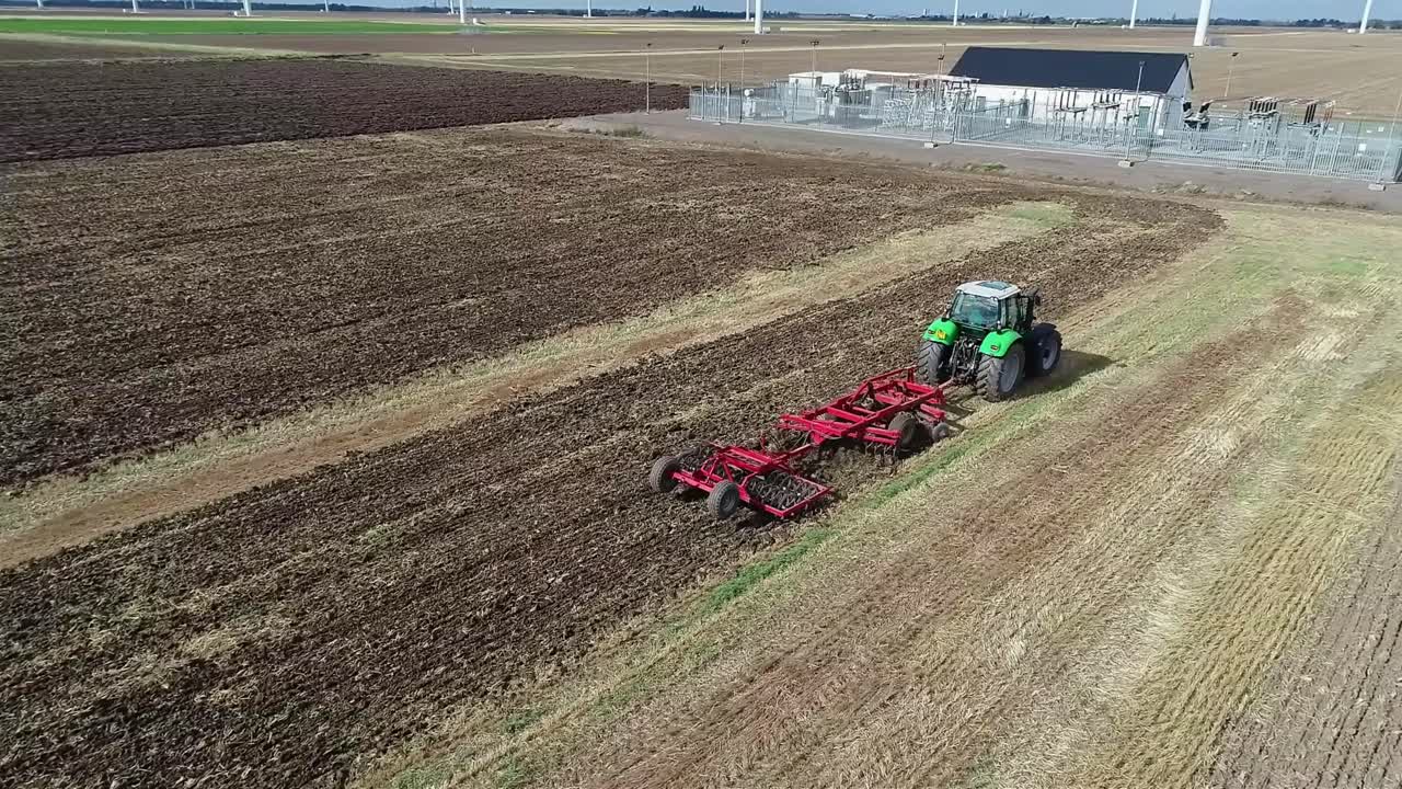 una vista aérea del dron mientras rodea un tractor que labra la tierra después de la cosecha y la prepara para la próxima cosecha