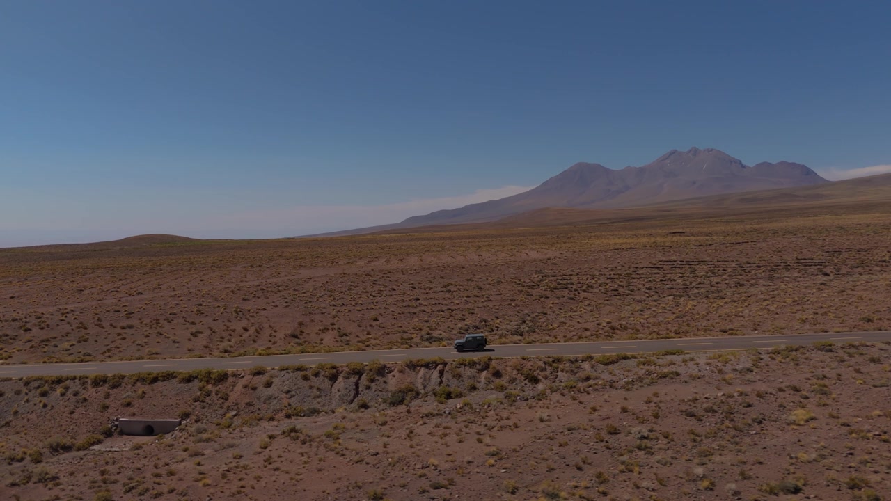 SUV compatto adatto al fuoristrada che guida lungo un'autostrada remota attraverso il paesaggio del deserto di Atacama, ripresa panoramica posteriore con drone