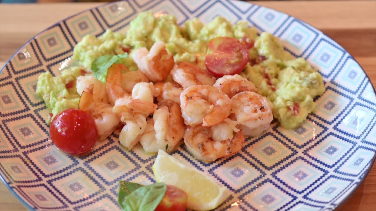 Close up of a plate with fried shrimp, tomatoes and guacamole on a plate