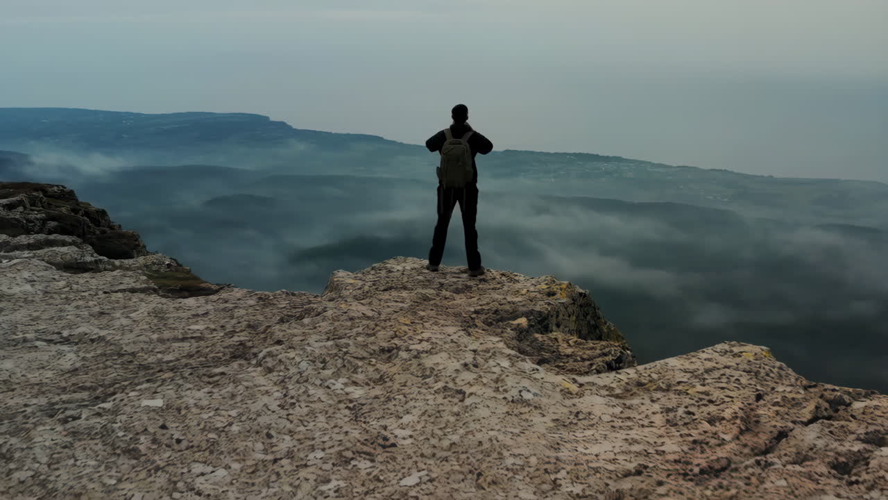 Hiker on a mountain peak overlooking a cloud-filled valley