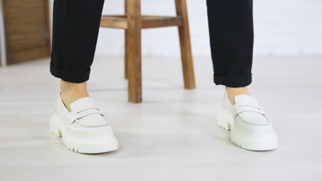 model wearing black trousers displays white new shoes on massive soles. close up. modern footwear presentation at white backdrop.