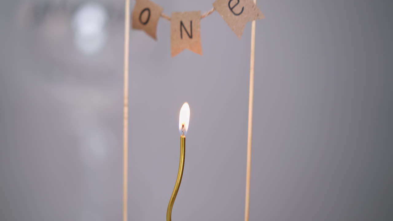 Thing curved golden candle burning on the white cake. Upper there is a sign "one year". Birthday cake close up.