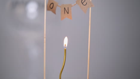 thing curved golden candle burning on the white cake. upper there is a sign "one year". birthday cake close up.