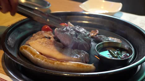 한식당에서 그릴에 소시지, 삼겹살, 토마토를 굽는 사람