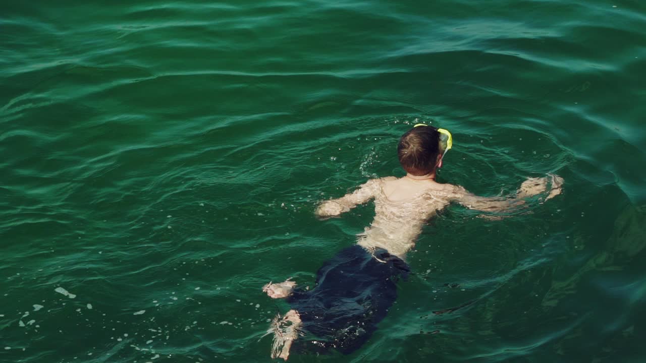 guy in blue shorts is swimming under water in a mask in the sea in the summer. Slow motion