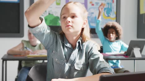 video of eager caucasian schoolgirl at desk raising hand and answering in diverse class, copy space