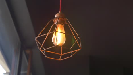 close-up of a vintage light bulb in a geometric cage hanging from the ceiling