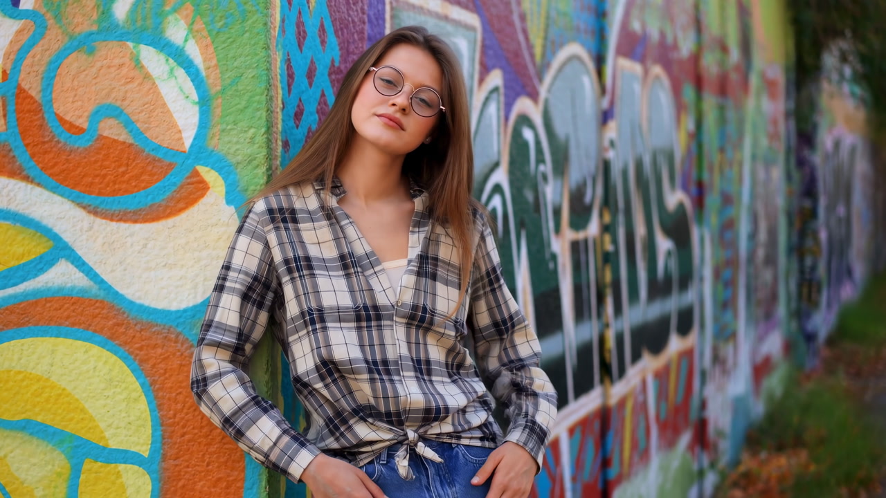 Young Woman Leaning On Graffiti Wall, Relaxed Smile, Plaid Shirt Tied At Waist, Highwaist Jeans, Round
