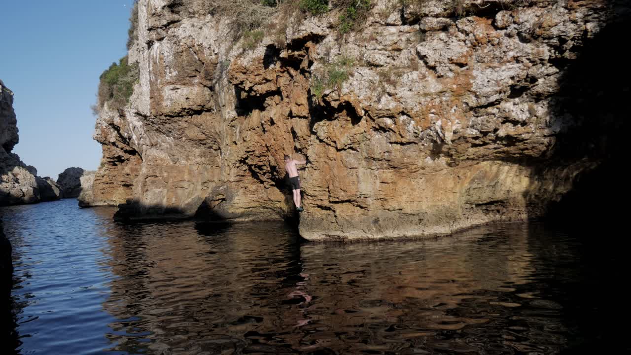 Climber scaling rocks by the water at Cala Rafalet, enjoying the outdoors and adventure