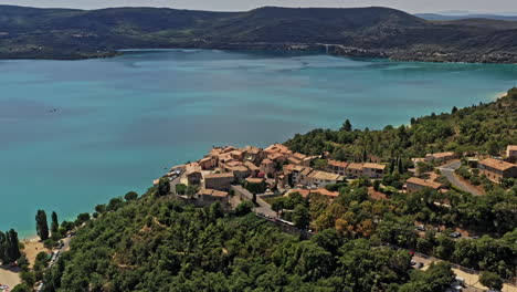 sainte croix du verdon francia antena v4 toma de establecimiento, dron vuela alrededor del pueblo de la ladera con vista al hermoso lago de sainte-croix con agua azul turquesa vívida rodeada de colinas - julio de 2021