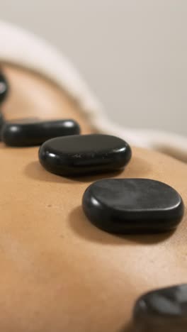 masseuse placing hot stones on client's back. vertical