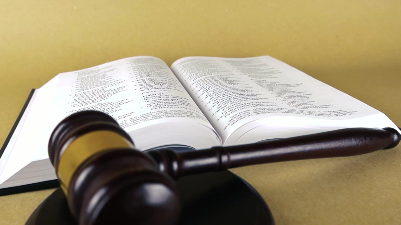 Wooden judge's gavel and sound block resting on the pages of an open Holy Bible, symbolizing the intersection of religious scripture, law, and moral judgment on a solid background