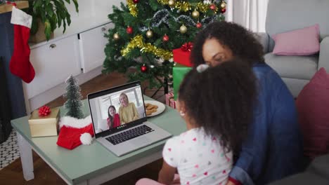 African-american-mother-and-daughter-on-video-call-with-female-friend-and-daughter-at-christmas-time