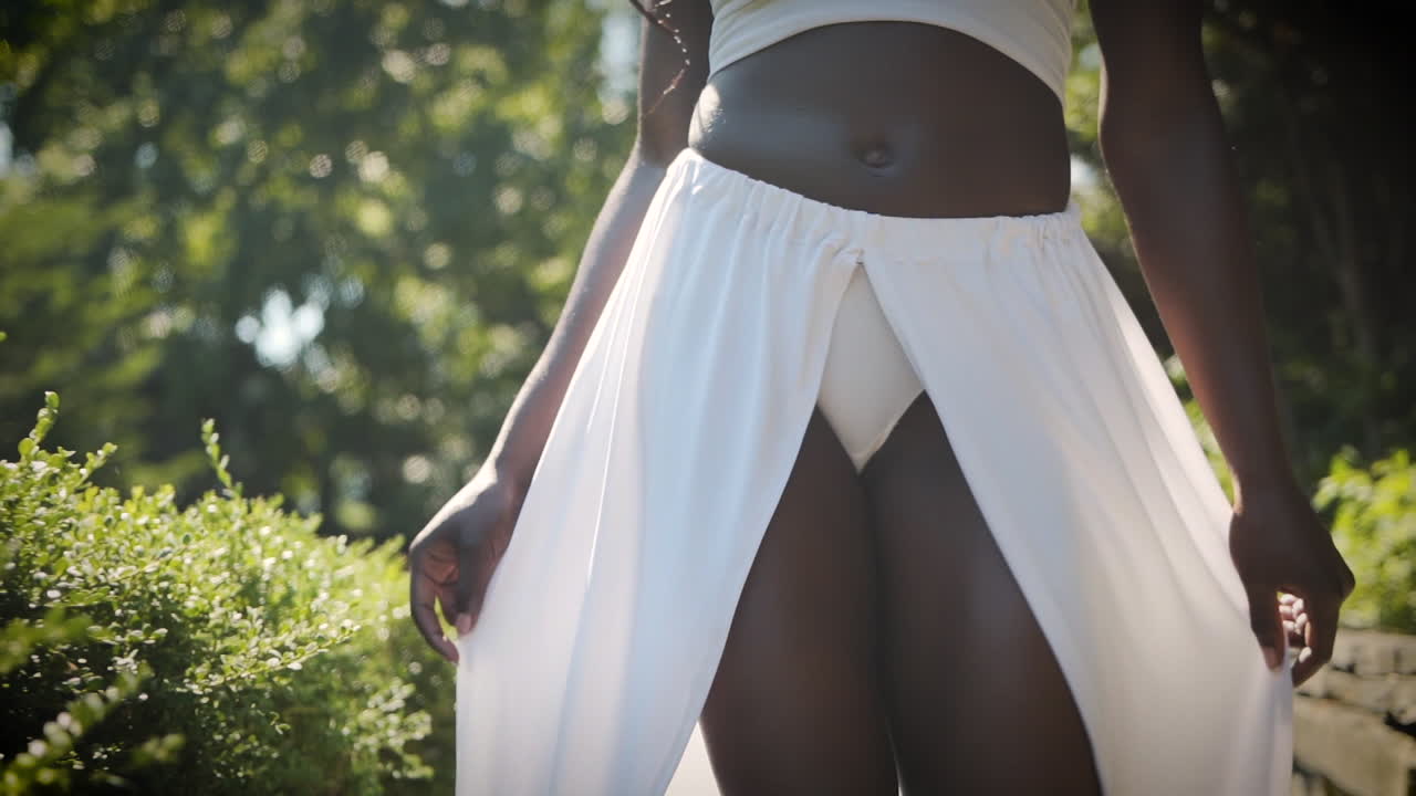 Bella donna che indossa un abito bianco e cammina in un parco al rallentatore.