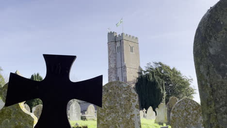 shot of a cross shaped grave stone in the foreground, and a church tower in the background