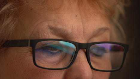 close up: elderly woman with glasses working on pc. eyes reflecting monitor