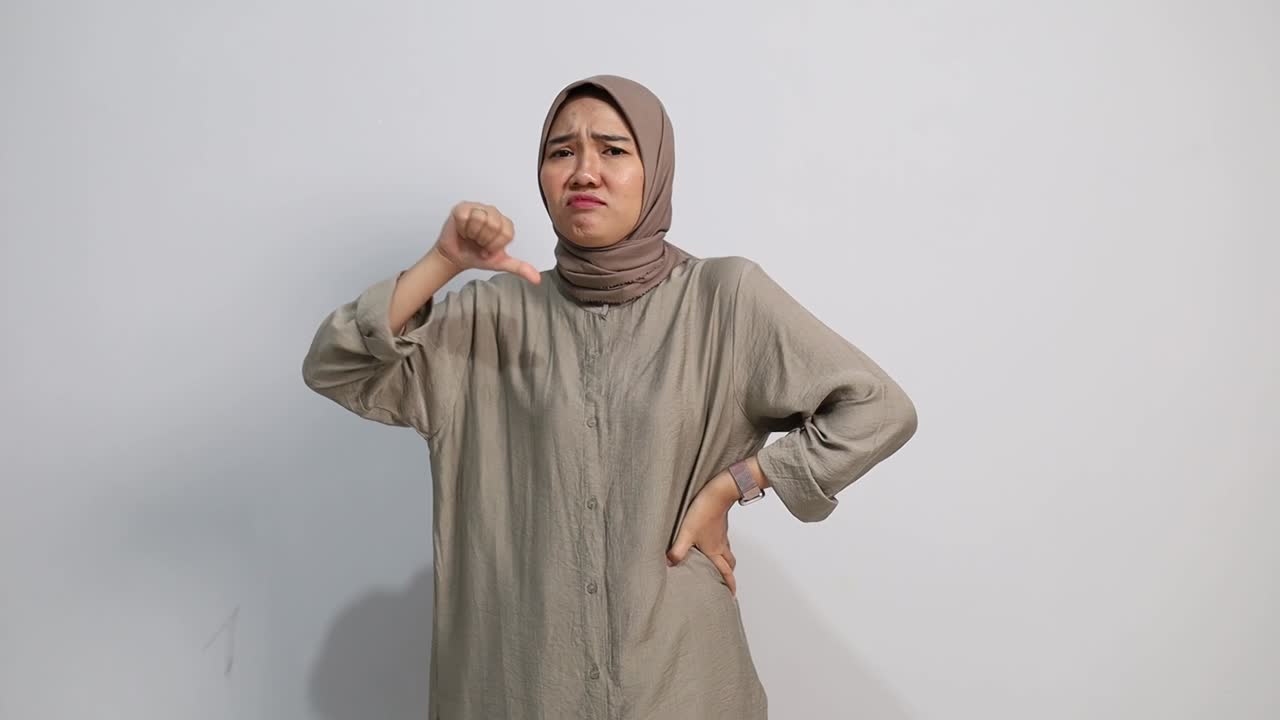 Wanita muslim Asia yang tidak puas menunjukkan jempol ke bawah dengan latar belakang putih