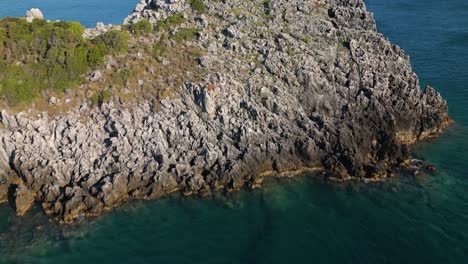 Aerial-dolly-above-sharp-jagged-cape-in-Corfu-Greece-to-reveal-blue-ocean-water