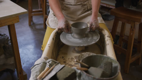 mid section of female potter using loop tool for finishing pottery at pottery studio