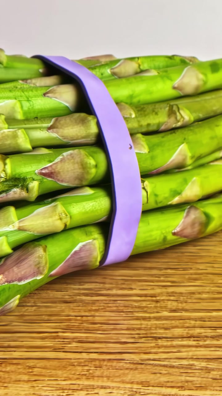 Close-up de lanças de aspargo verde vibrante amarradas com uma faixa roxa em uma superfície de madeira. Ótimo para blogs de culinária ou conteúdo gastronômico.