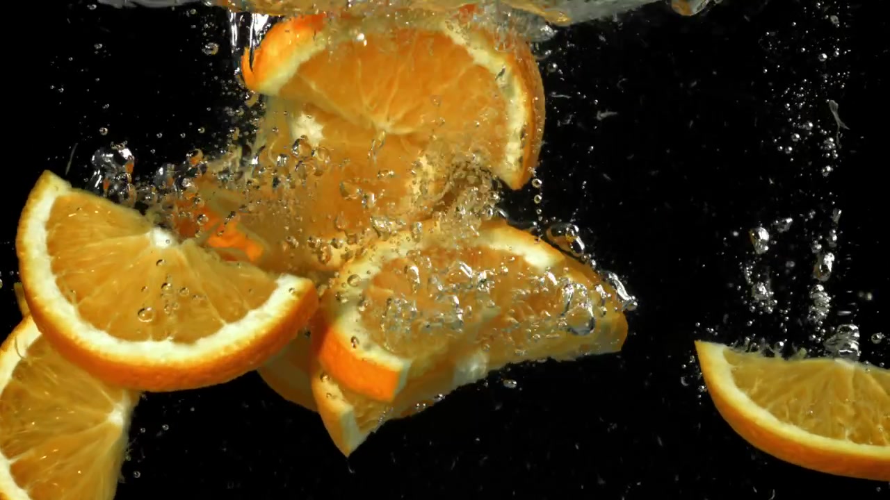Fette d'arancia fresche che schizzano nell'acqua al rallentatore