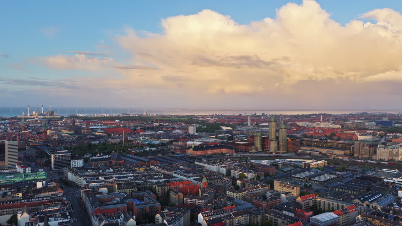 Aerial drone view of Copenhagen, Denmark with historic towers, modern buildings, and red rooftops under a bright morning sky