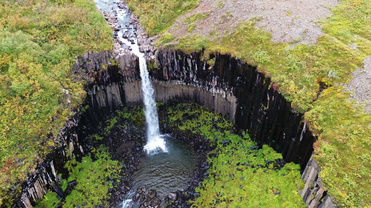 Drönarvy över Svartifoss vattenfall som kaskaderar nerför dramatiska basaltpelarklippor i Vatnajökulls nationalpark, Island.