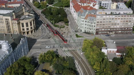Dos-Tranvías-Rojos-Cruzando-La-Intersección-En-Bratislava,-Eslovaquia,-Tiro-Aéreo-En-Verano-Soleado